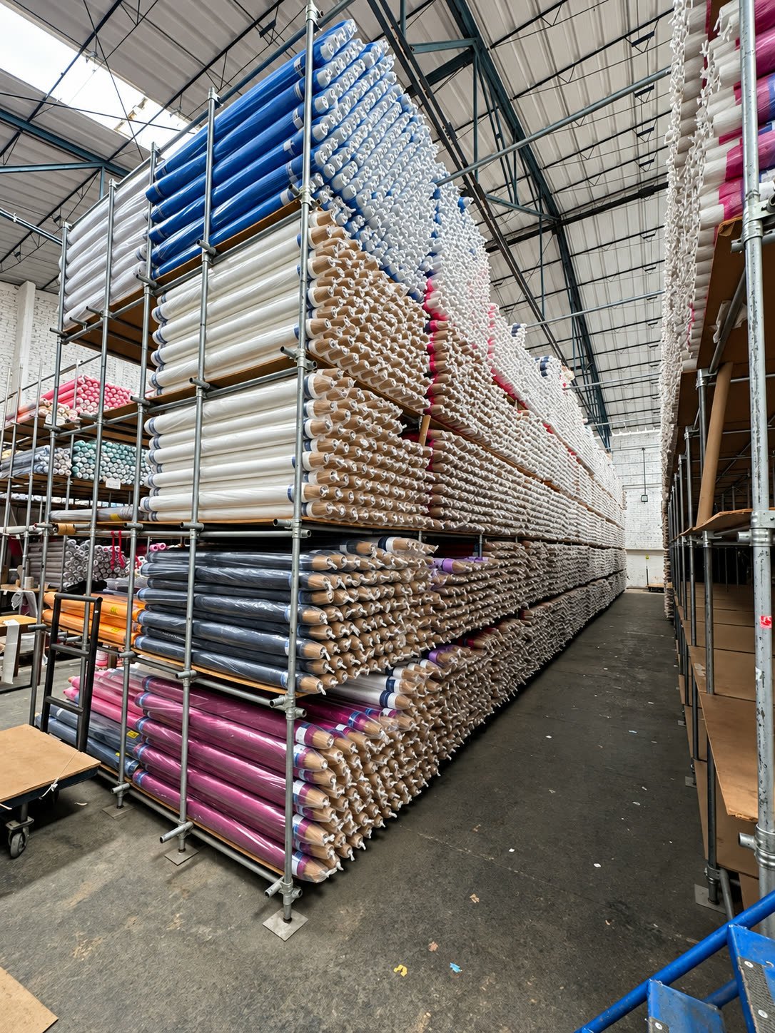 Rack metálico de varios niveles con rollos de tela apilados en un almacén